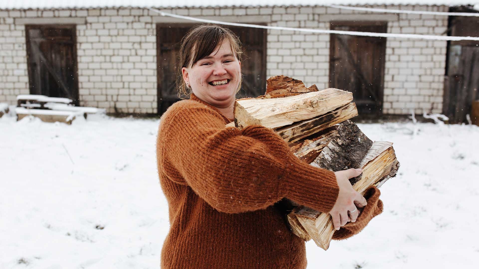 A lady carrying wood for the fire through snow.