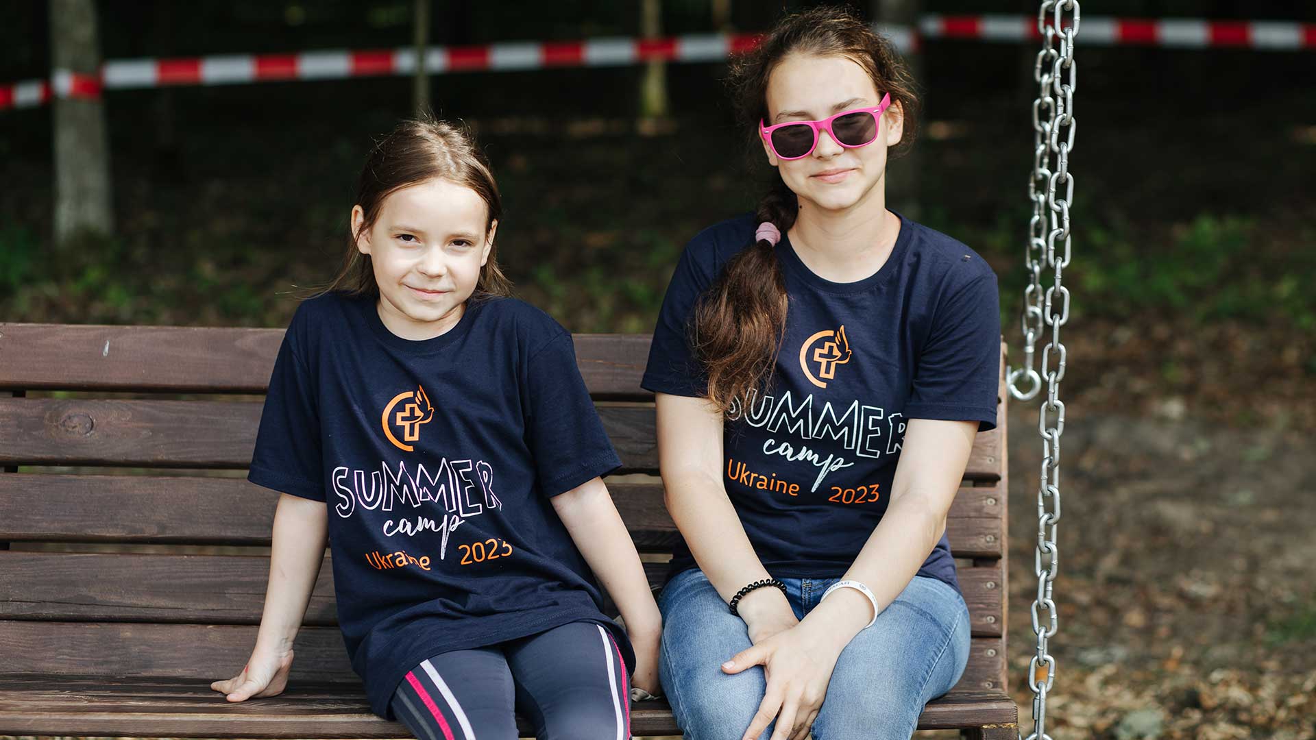 Two girls sit on a swing at summer camp.