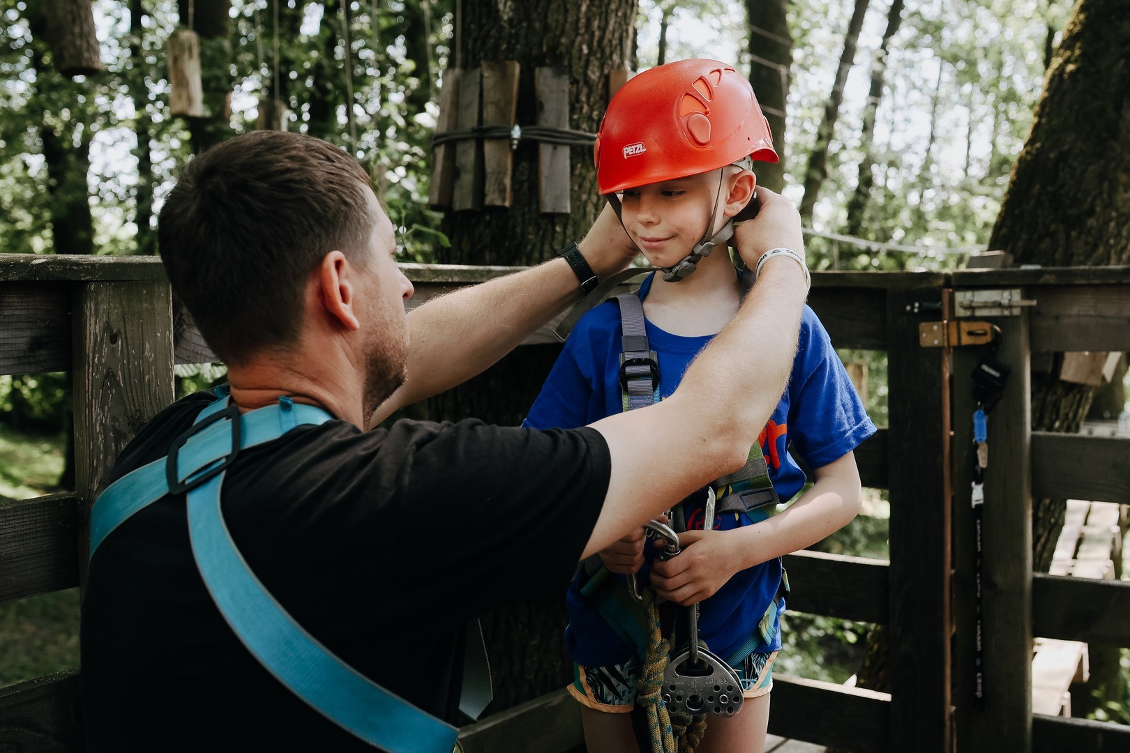 A young boy is helped into a helmet and climbing harness.