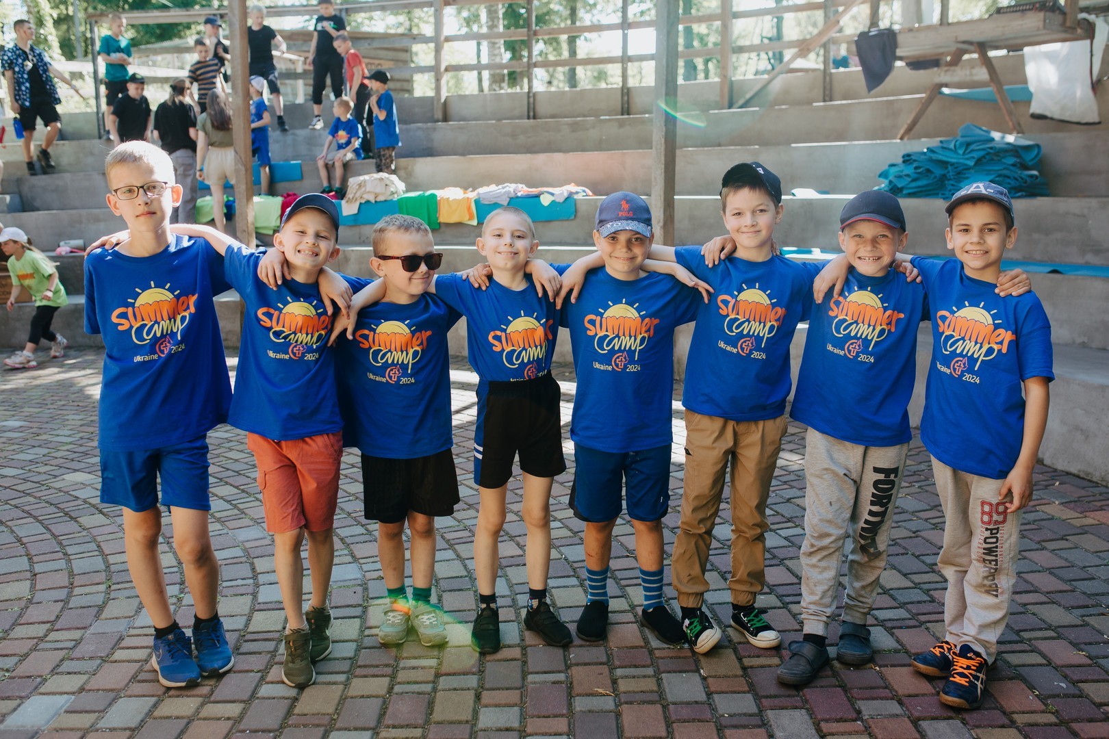 A row of boys wearing summer camp shirts smile at the camera.