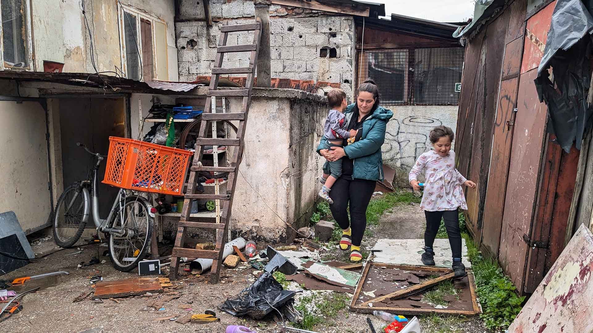 A mother and her two children walking over rubble outside their home.