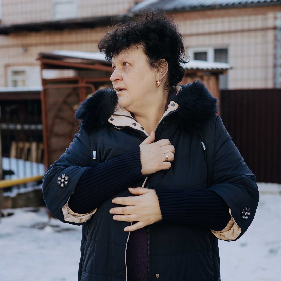 A lady stands outside in the snow, wearing a warm coat.