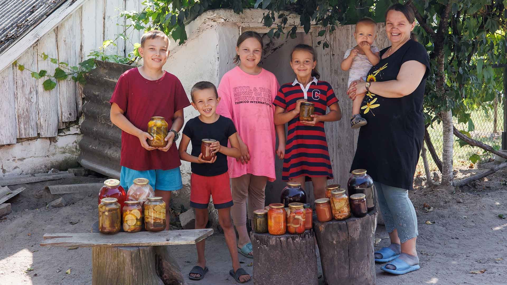 A family stand smiling with jars of produce they've grown.