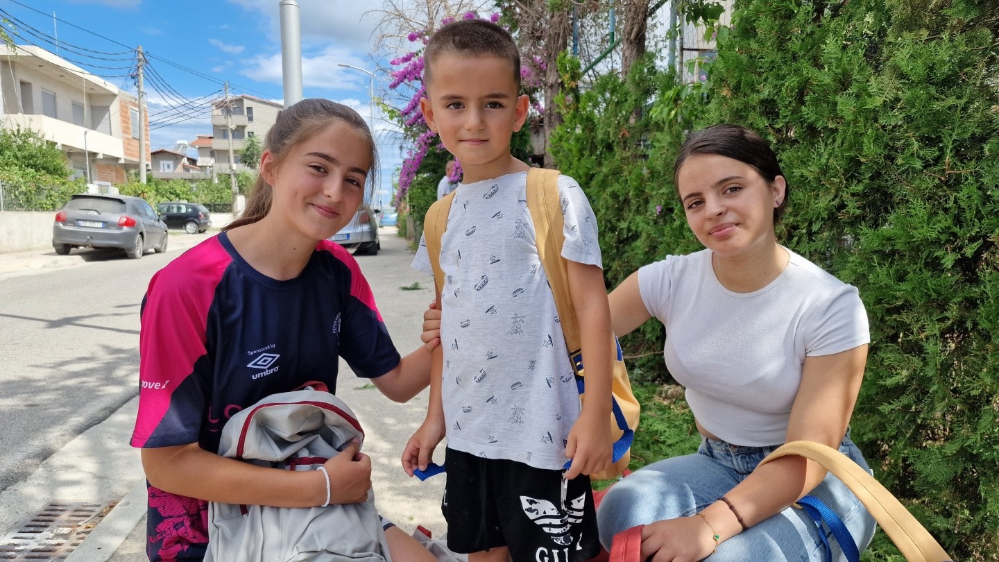 A young boy stands with his two sisters, wearing his new backpack.