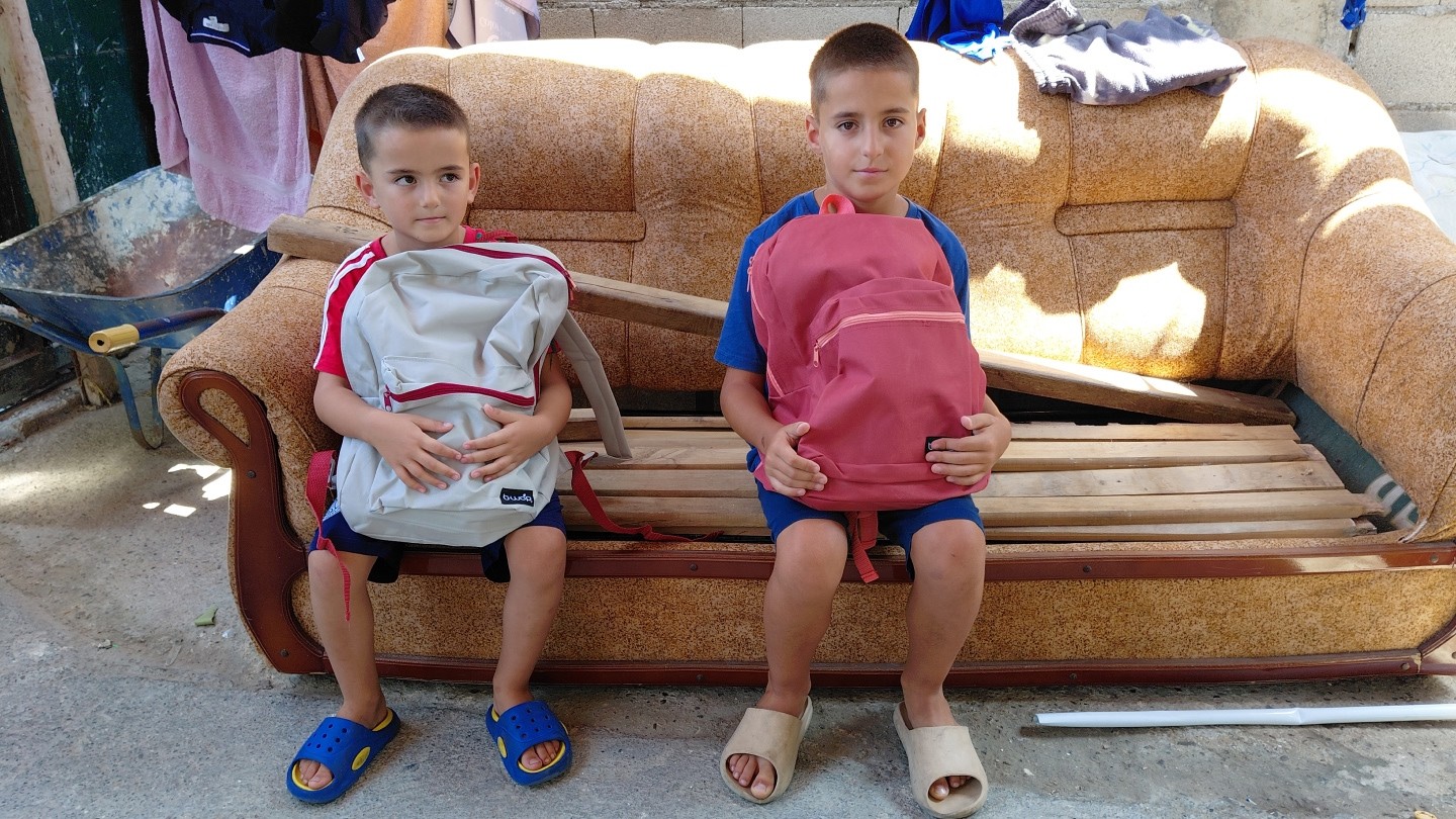 Two boys sit with their new backpacks.